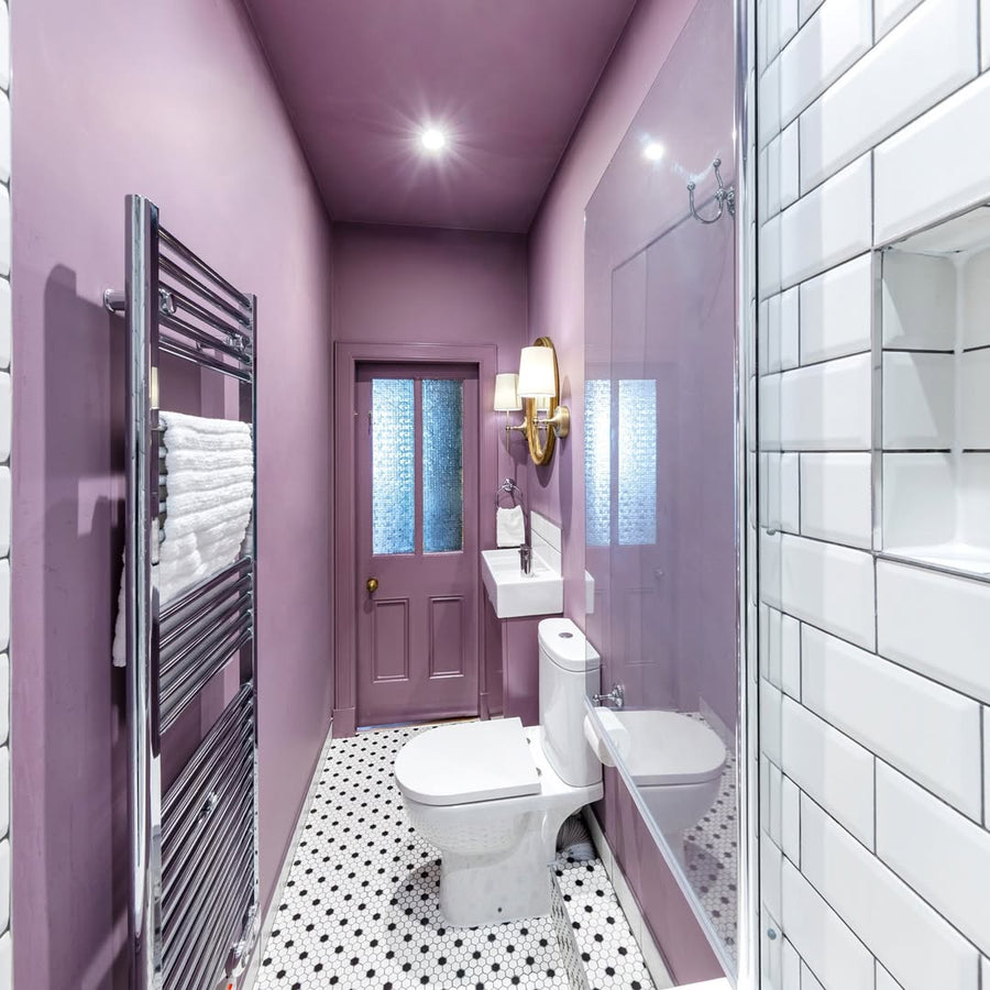Compact Edinburgh tenement bathroom by Forazzi Bathrooms — Omnitub Deluxe 1700 × 750mm white deep soaking tub at the far end of a narrow bathroom with deep mauve walls, brass sconce and monochrome hexagonal floor tiles — handmade in Britain