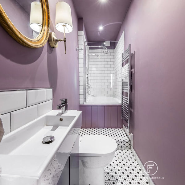 Glass shower screen and chrome heated towel rail alongside an Omnitub Deluxe 1700 × 750mm white deep soaking tub with deep mauve tongue-and-groove panelling in narrow Edinburgh tenement bathroom by Forazzi Bathrooms