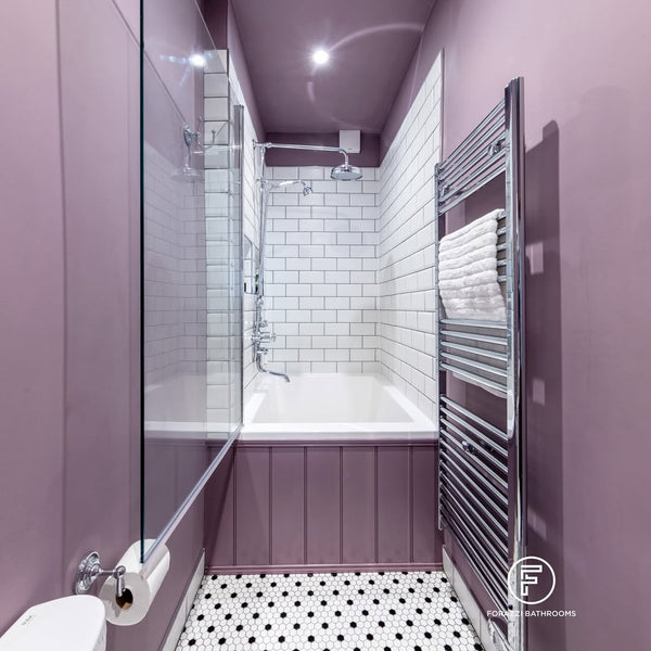 Omnitub Deluxe 1700 × 750mm white deep soaking tub tucked into the end of a narrow Edinburgh tenement bathroom — glass shower screen, chrome heated towel rail and deep mauve tongue-and-groove panelling — handmade in Britain