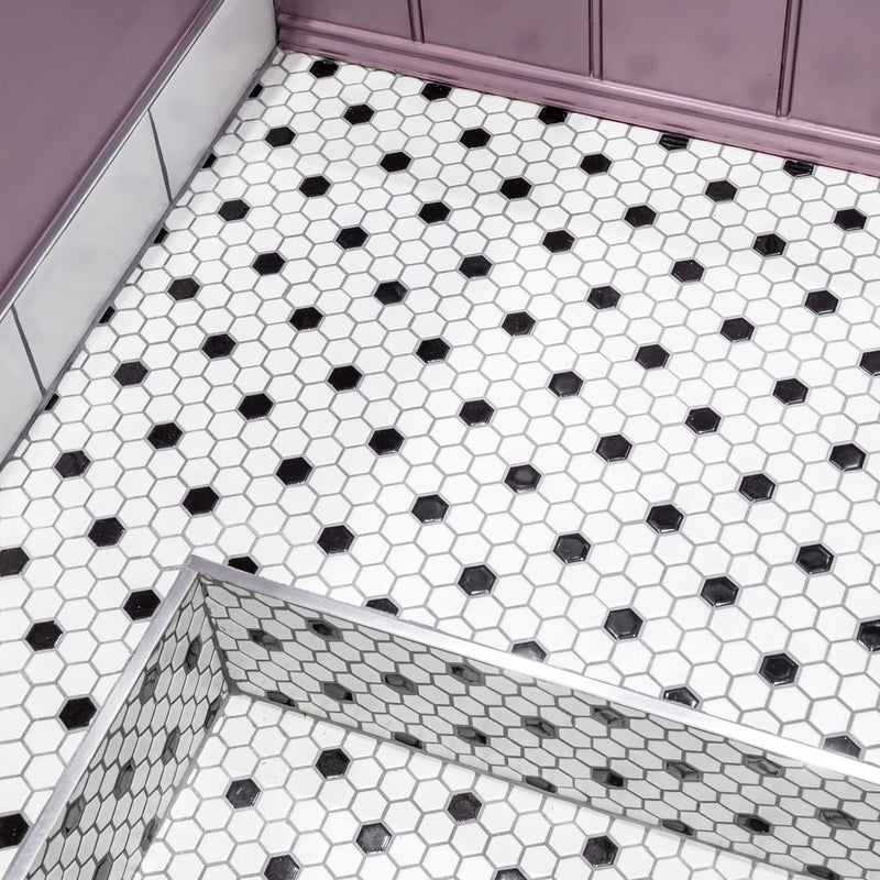 Black and white hexagonal mosaic floor tiles meet the mauve tongue-and-groove bath panel. The glass shower screen reflection shows just how deep this tub sits.