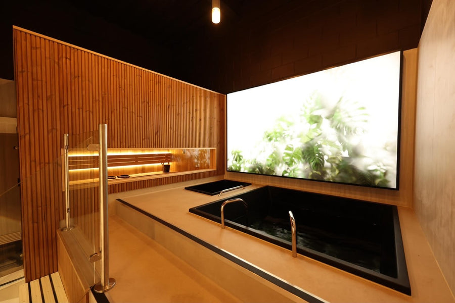 The seated tub set into micro-cement, botanical light-wall behind