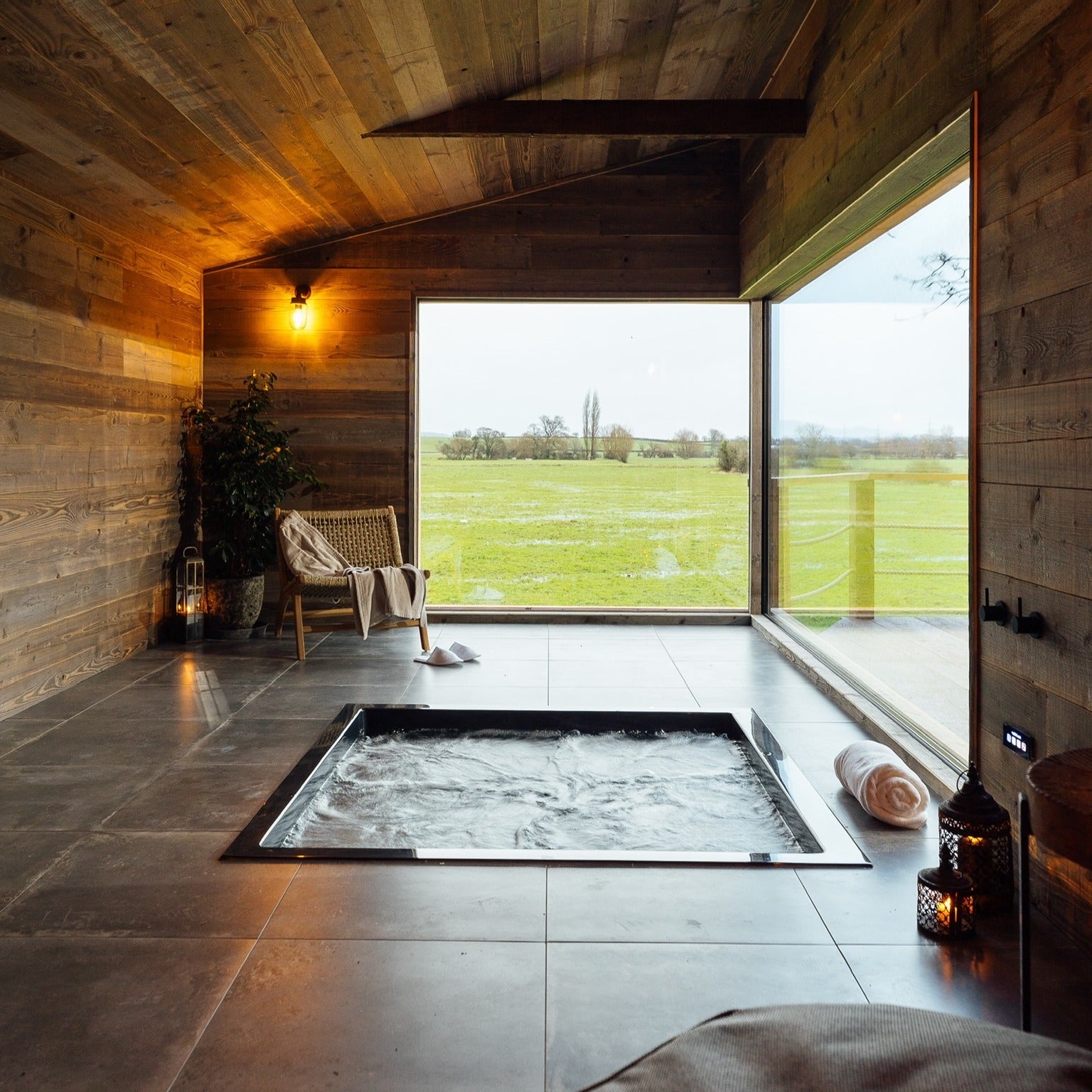 Sunken 1600 x 1600 Omnitub, filled and flush with the tiled floor of a timber-clad bathroom, beneath a corner picture window over open fields